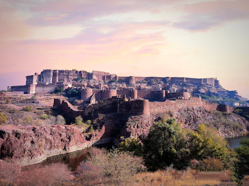 An ancient fort perched on a rocky hill, overlooking a serene desert landscape at sunset.