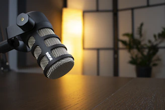 A microphone with headphones resting on a wooden table, bathed in warm studio light.