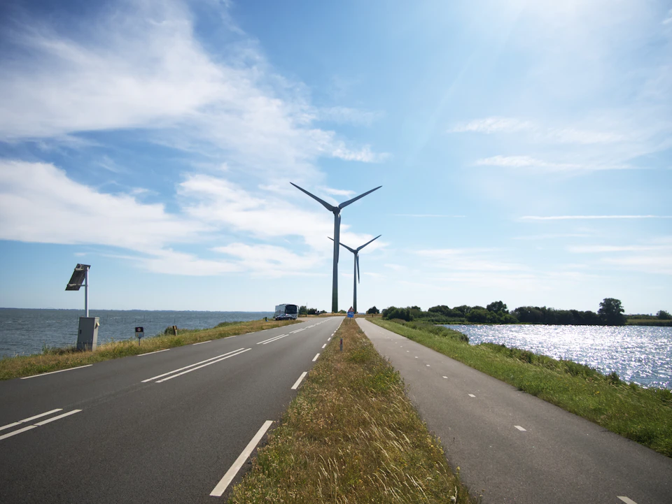 Two large wind turbines stand on either side of a winding road through landscape