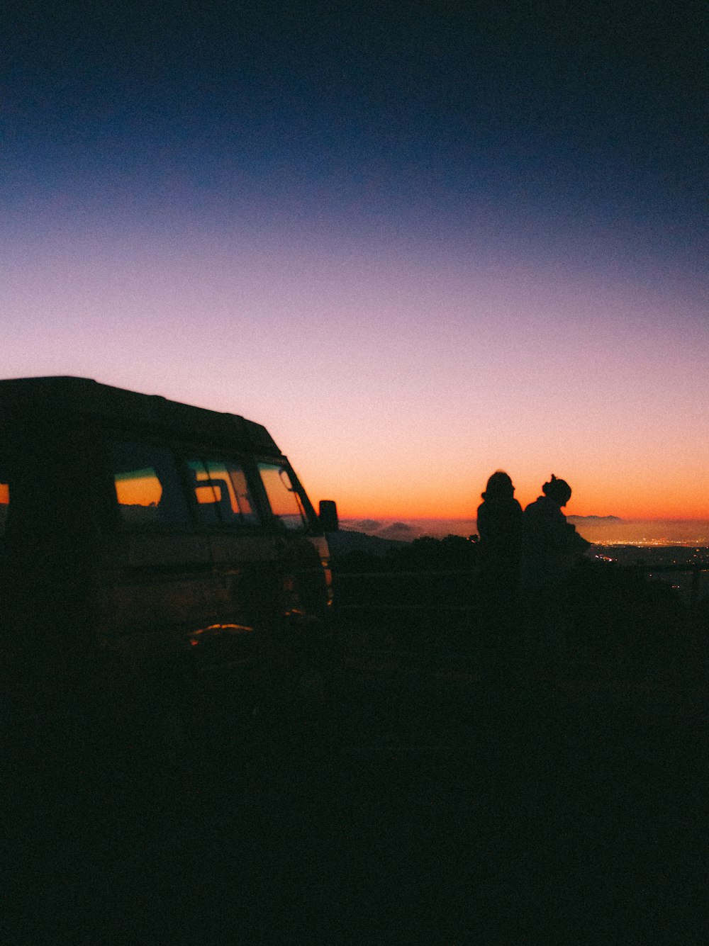 a couple of people sitting on a car in front of a sunset