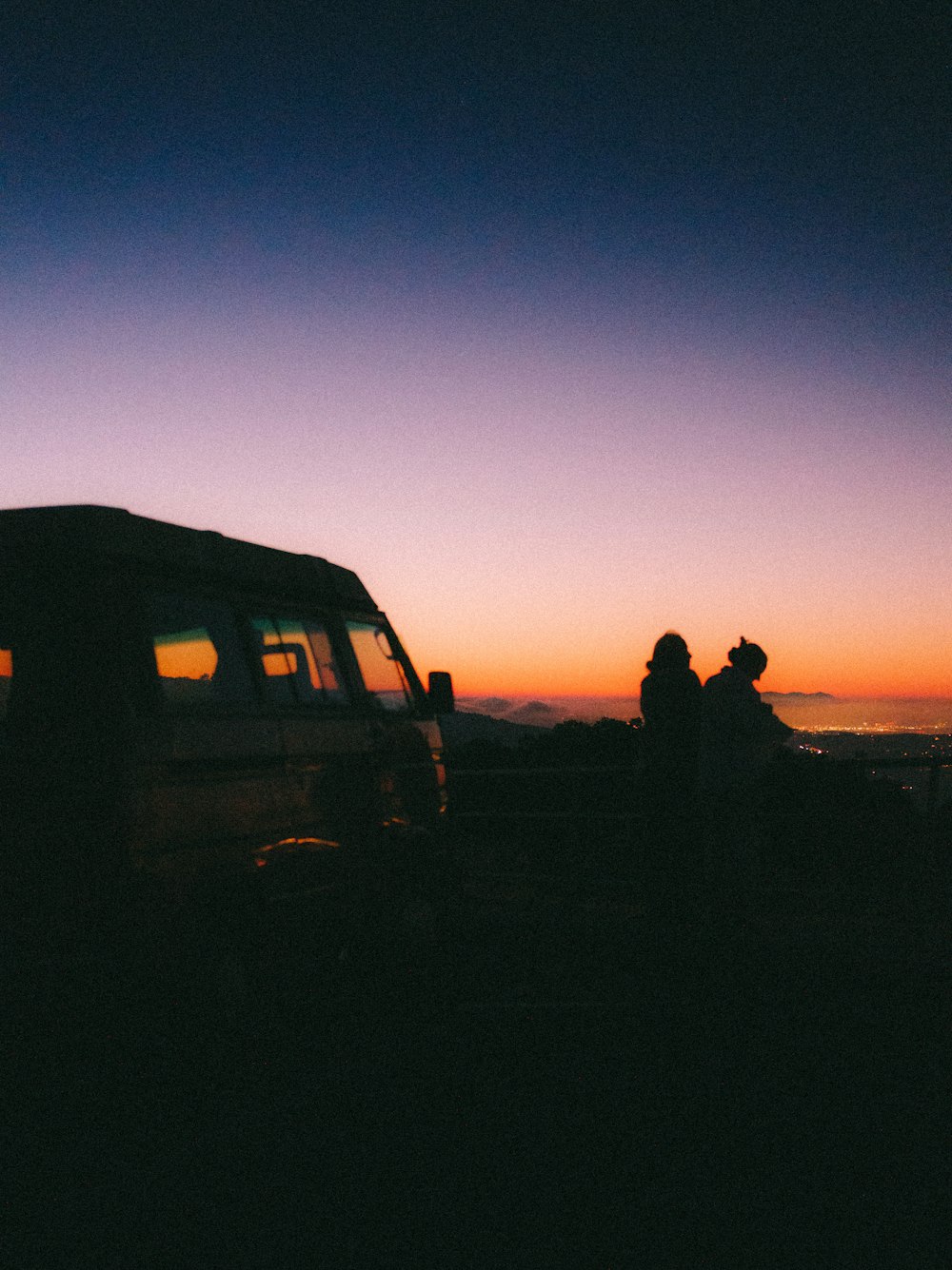 um casal de pessoas sentadas em um carro em frente a um pôr do sol