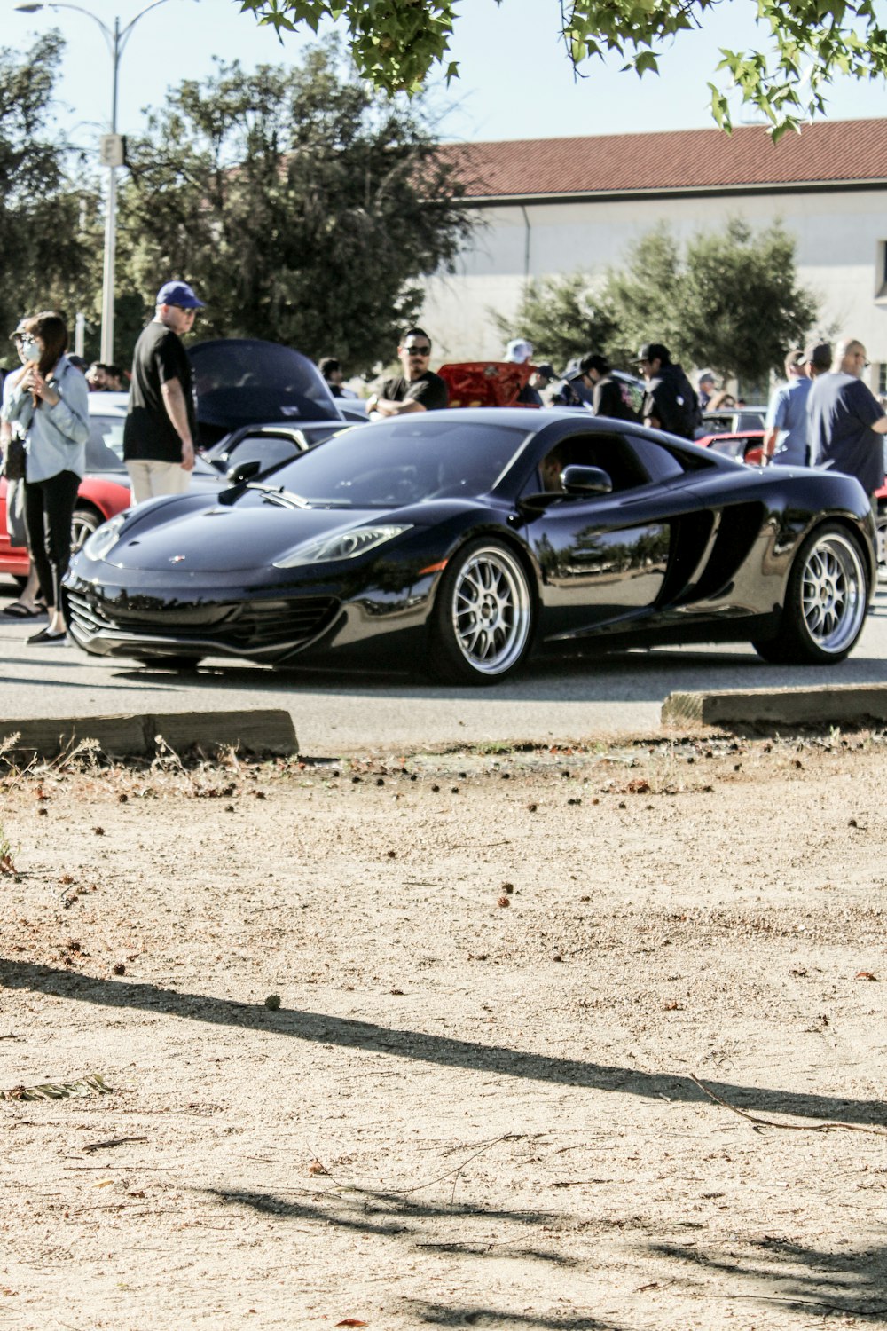 a black sports car parked on the side of a road with people standing around