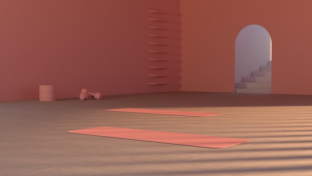 A minimalist room with a warm, peach-colored palette. Two yoga mats are laid out on the floor, with soft lighting casting shadows. In the background, there are shelves with a few items and a set of stairs leading to an arched doorway.