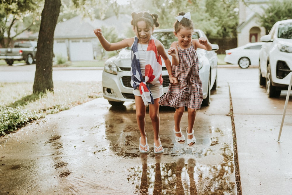 two girls in dresses and ties running in a puddle