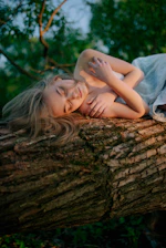 A serene woman sitting barefoot on soft earth, eyes closed, surrounded by natural light filtering through trees.