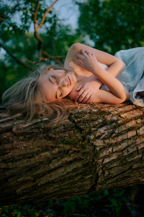 A serene woman sitting barefoot on soft earth, eyes closed, surrounded by natural light filtering through trees.