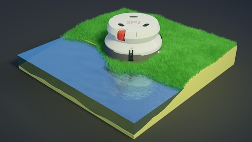 A small 3D model represents a section of terrain with green grass and a body of water. On the grassy area, there is a round, white robotic device with red and black accents. The surface of the water reflects the light, creating a realistic appearance.