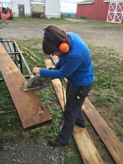 A craftsman using a Milwaukee circular saw cutting through a thick wooden plank outdoors.