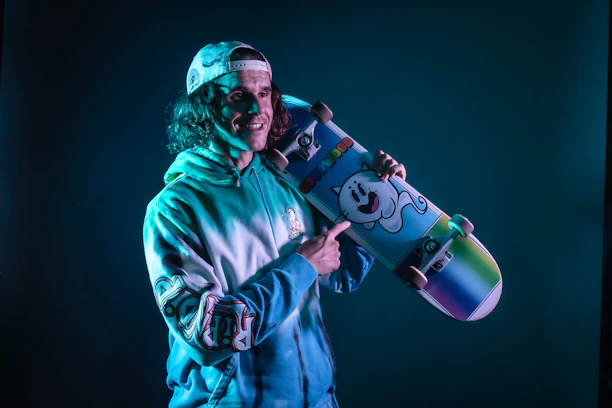 A happy customer wearing a Saltride hoodie, holding their new skateboard in front of a Salt Lake City mural.