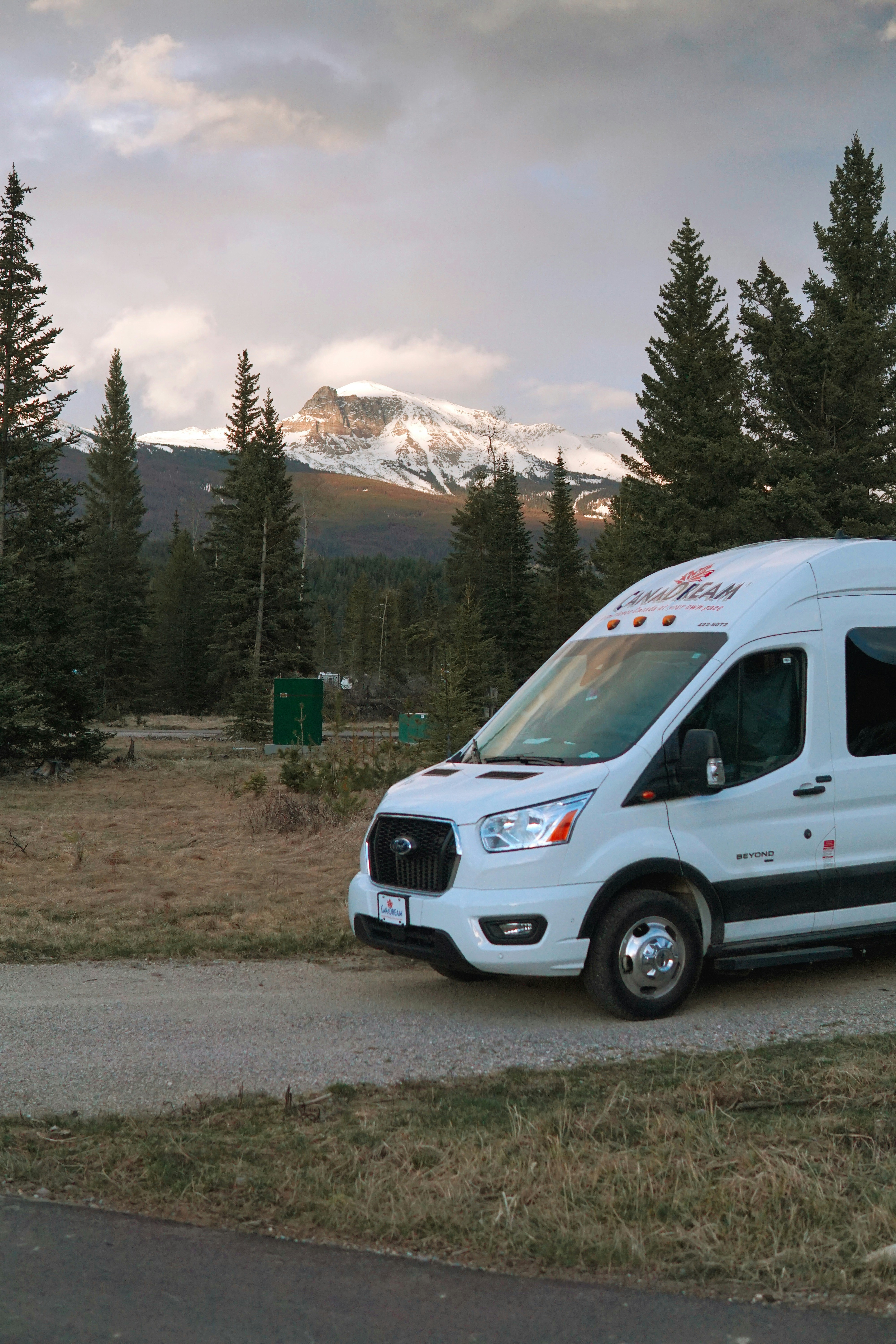 A white van parked on a road with trees and a mountain in the ...