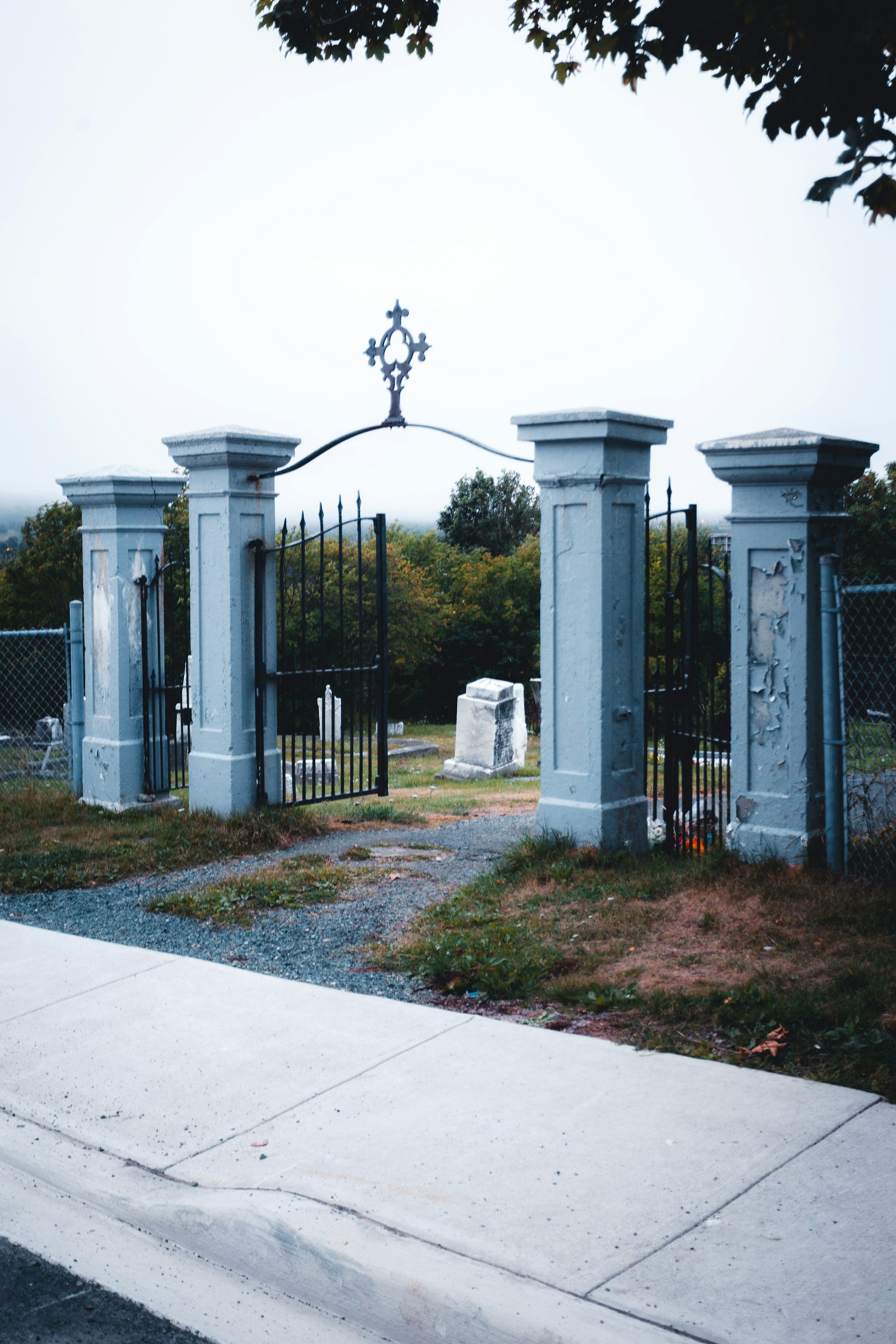 An ancient, weathered graveyard gate creaking open under a cloudy sky, with faint glowing orbs hovering among the tombstones.