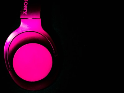 A bright pink headphone with one earcup visible against a black background, featuring a metallic sheen and a logo on the headband.