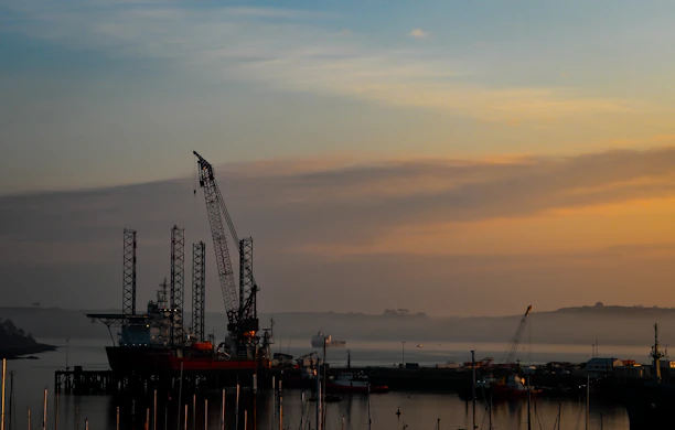 A panoramic view of an offshore oil platform at sunset, highlighting the calm sea and steady operations.