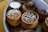 Small clay pots filled with various grains and seeds are arranged on a tray. Some pots contain popped sorghum, while others hold different grains and nuts. A rolled-up paper or cloth is tucked to the side.