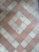 A floor composed of diamond-shaped tiles arranged in an alternating pattern of reddish-brown and beige colors. The surface of the tiles shows some wear and small debris, indicating use over time.