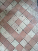 A floor composed of diamond-shaped tiles arranged in an alternating pattern of reddish-brown and beige colors. The surface of the tiles shows some wear and small debris, indicating use over time.