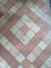 A floor composed of diamond-shaped tiles arranged in an alternating pattern of reddish-brown and beige colors. The surface of the tiles shows some wear and small debris, indicating use over time.