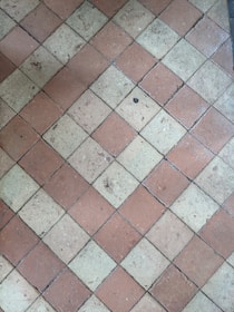 A floor composed of diamond-shaped tiles arranged in an alternating pattern of reddish-brown and beige colors. The surface of the tiles shows some wear and small debris, indicating use over time.