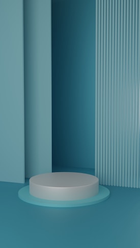 A minimalist scene with a white circular platform set against a modern background of vertical ridged panels and smooth surfaces in varying shades of teal.