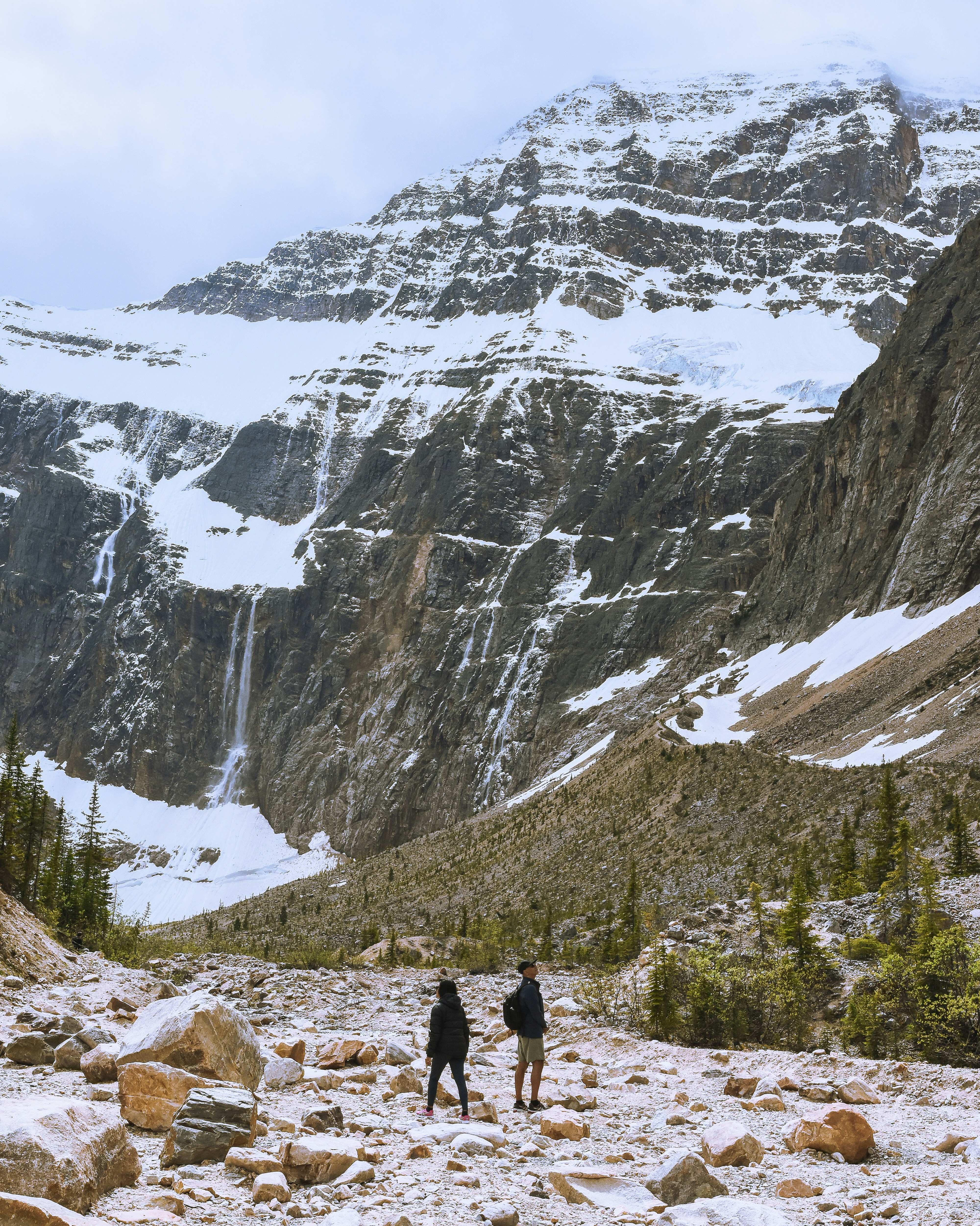 a couple people walking on a rocky trail in front of a mountain