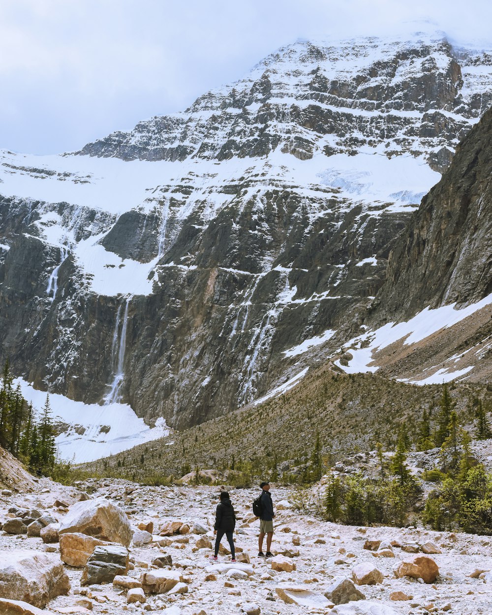 a couple people walking on a rocky trail in front of a mountain