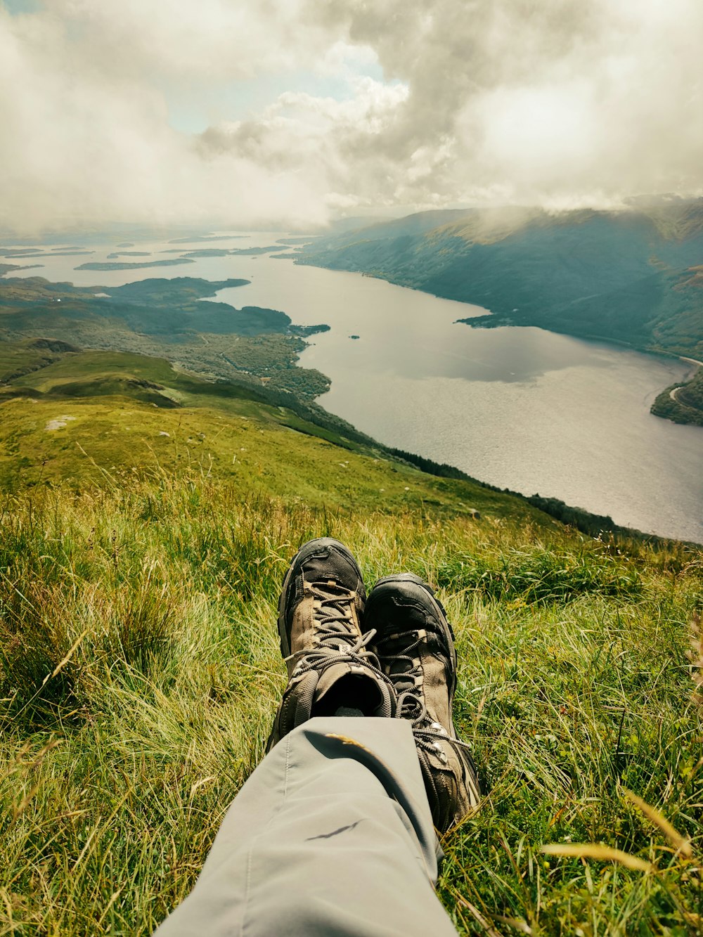 a person's feet on a grassy hill overlooking a body of water