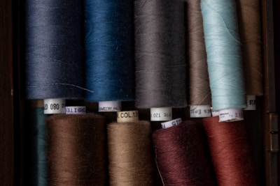 Several spools of thread in various colors are neatly arranged in a grid. The spools have labels with numbers and text and appear to be made of a glossy material.