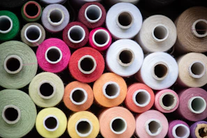 Close-up of colorful polyester spun thread spools lined up in a factory.