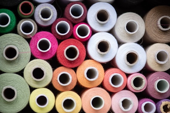 Various colorful spools of thread arranged closely together, showcasing a wide range of colors including green, pink, red, orange, and white. The spools are viewed from above, emphasizing the circular shapes of the thread wrapped around them.