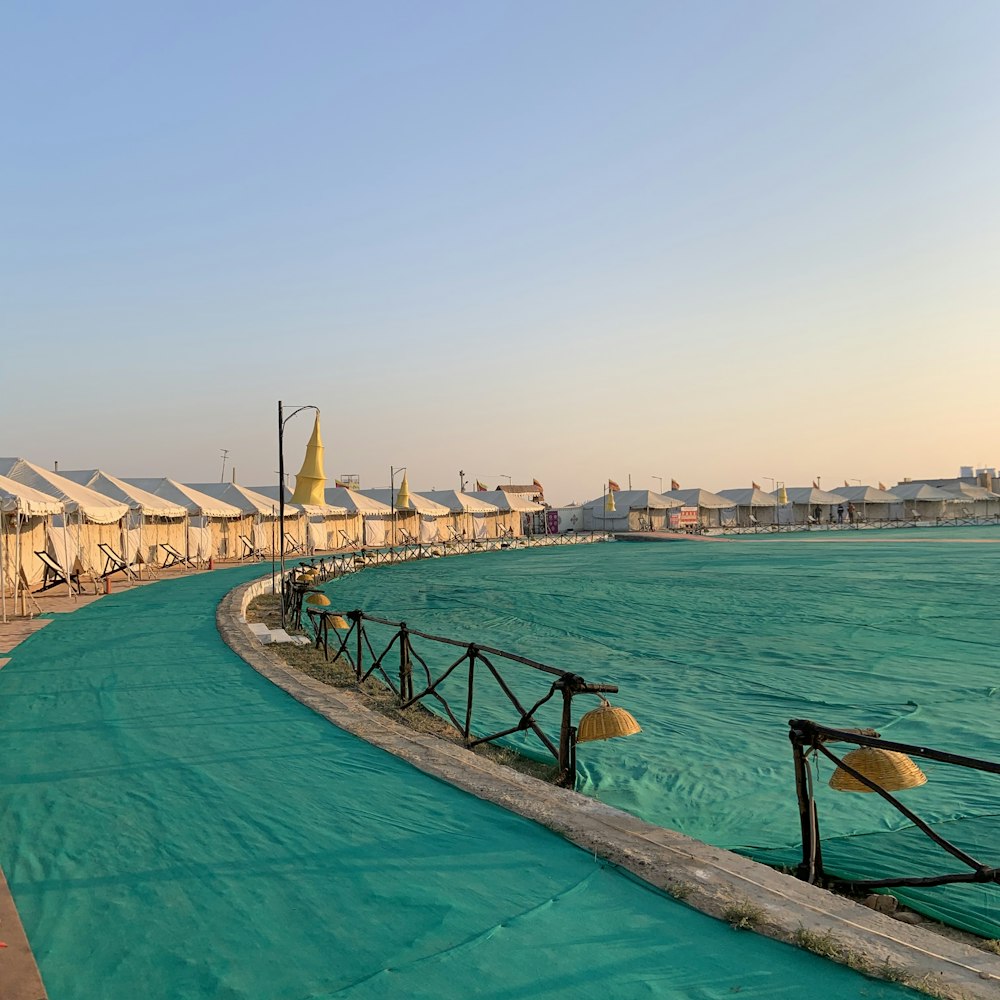 a pool with a walkway and a beach with buildings in the background