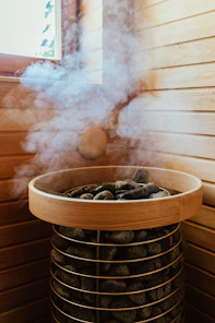 Steam rising from hot dark stones in a wooden sauna heater