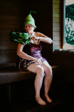 A serene woman sitting comfortably in a cedar steam barrel surrounded by soft natural light and gentle steam.