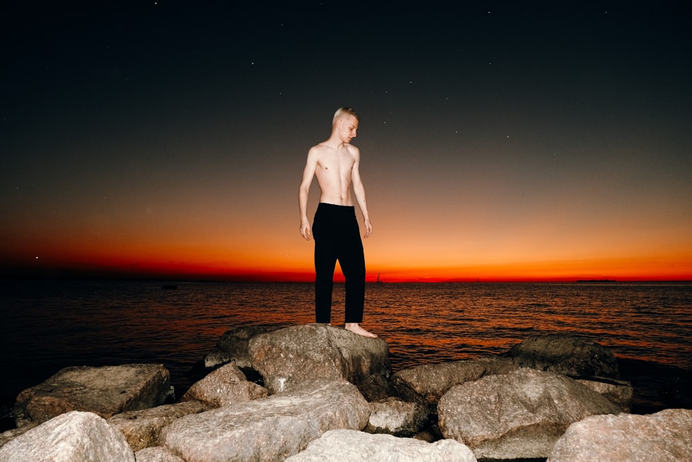 a man standing on rocks by the water at sunset