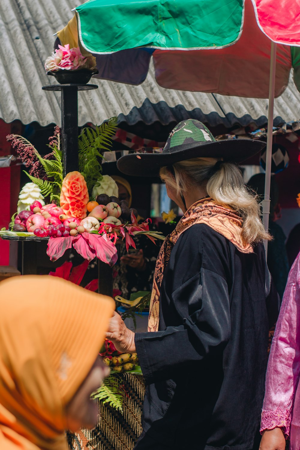 a woman in a hat looking at a fruit stand