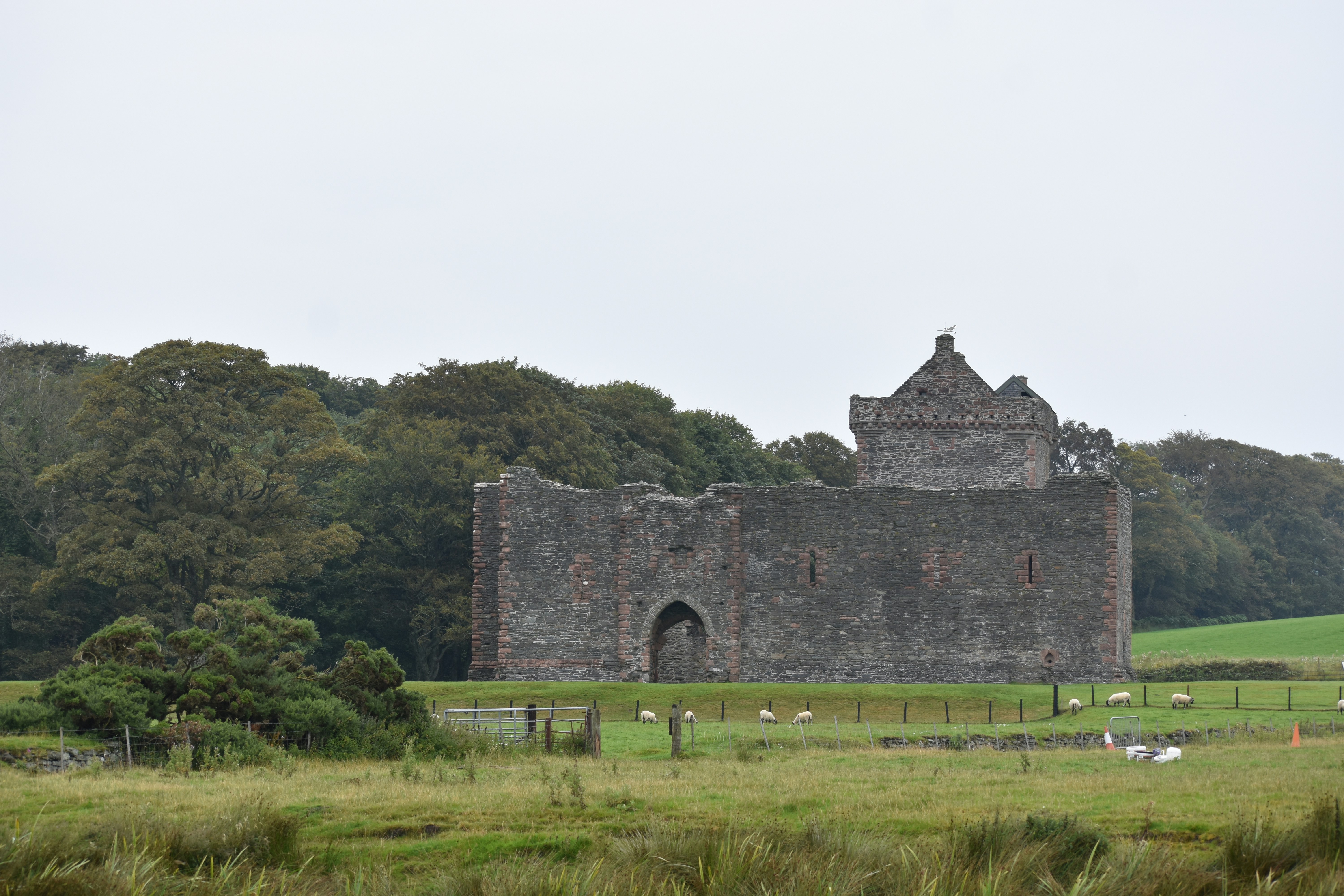 a stone building with a fence and trees in the background, 