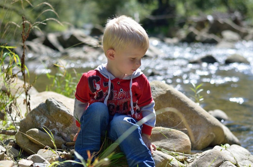 a child sitting on a rock by a river