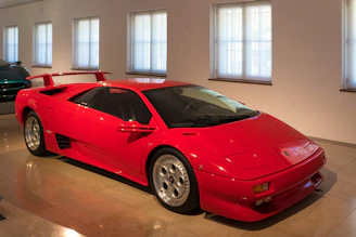 A gleaming red sports car being carefully polished by a technician under natural sunlight.