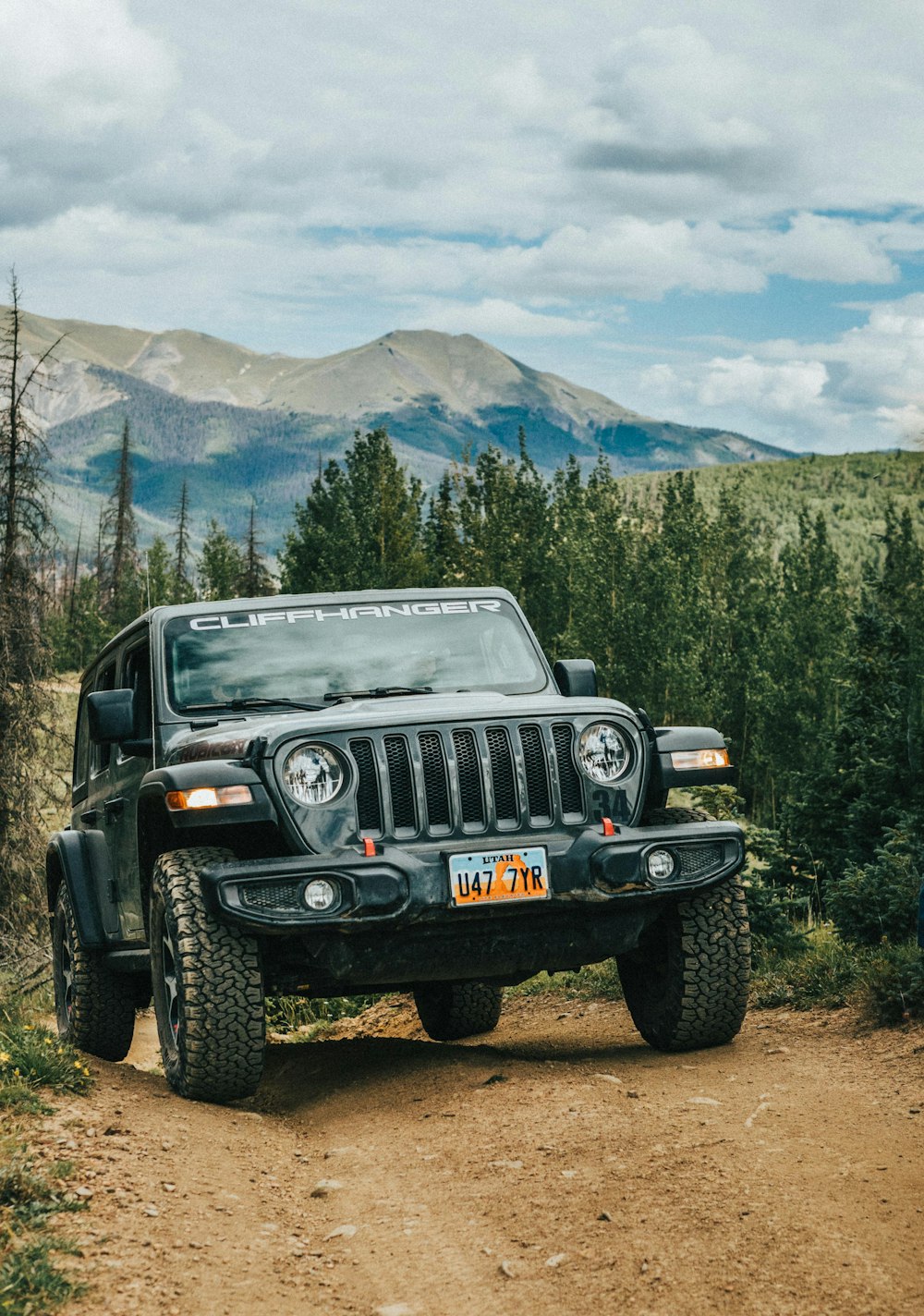 a jeep parked on a dirt road with trees and mountains in the background