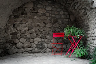 a red chair and a plant in front of a stone wall