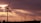 Tall wind turbines stand against a backdrop of a dramatic sunset sky, with sunlight piercing through scattered clouds. The silhouetted turbines create a serene yet striking image, emphasizing both the grandeur of the sky and the elegance of renewable energy structures.