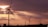 Tall wind turbines stand against a backdrop of a dramatic sunset sky, with sunlight piercing through scattered clouds. The silhouetted turbines create a serene yet striking image, emphasizing both the grandeur of the sky and the elegance of renewable energy structures.