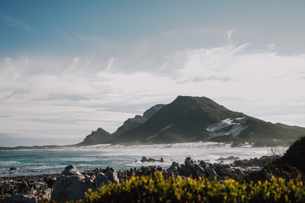 a rocky beach with a large body of water and a mountain in the distance