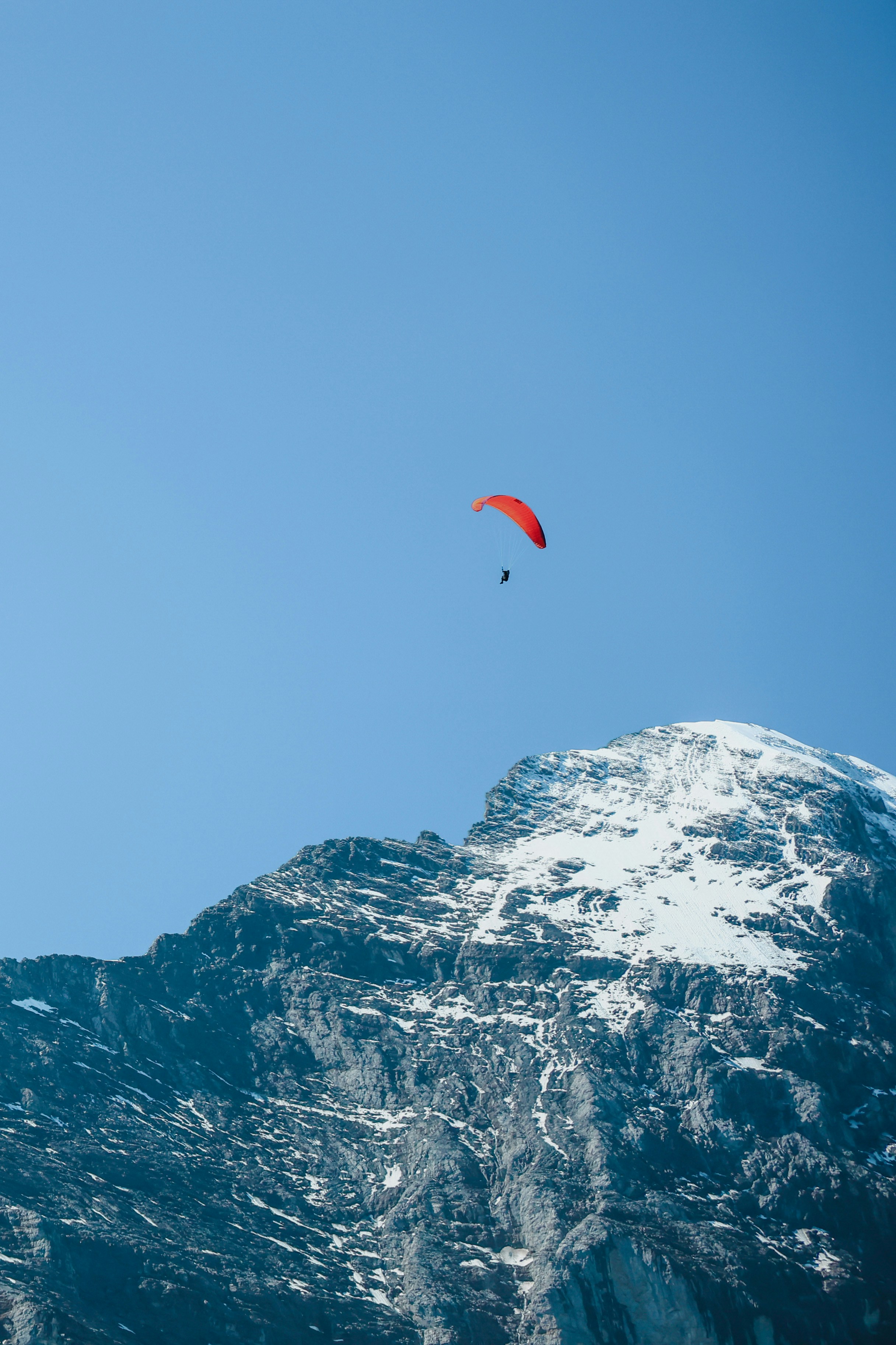 une personne dans les airs avec un parachute au-dessus d’une montagne enneigée