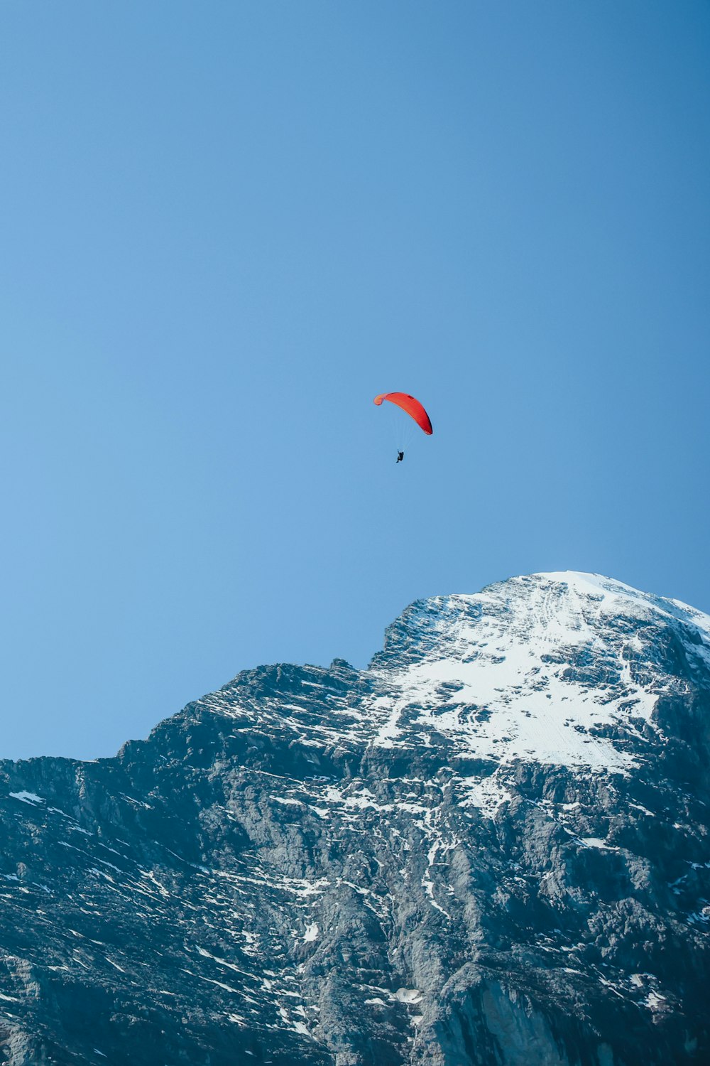 a person in the air with a parachute above a snowy mountain