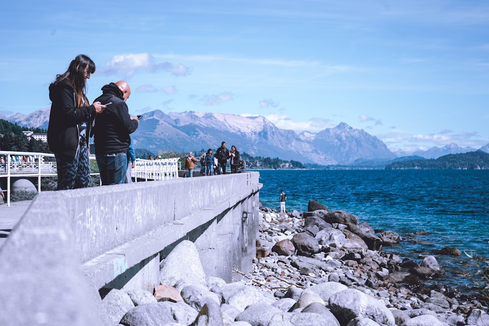 a man and woman kissing on a rocky shore with water and mountains in the background