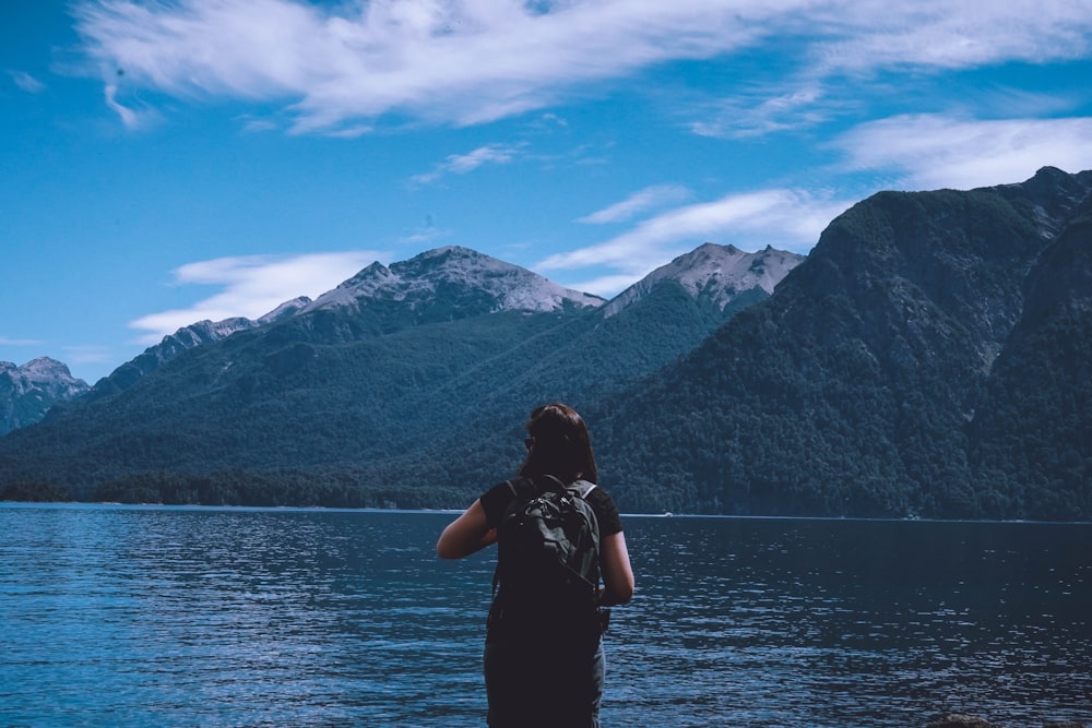 um homem em pé na frente de um lago com montanhas ao fundo