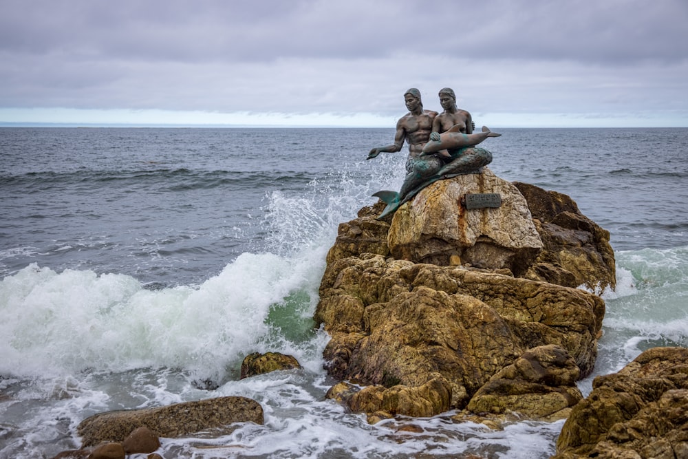 two people sitting on a rock in the ocean