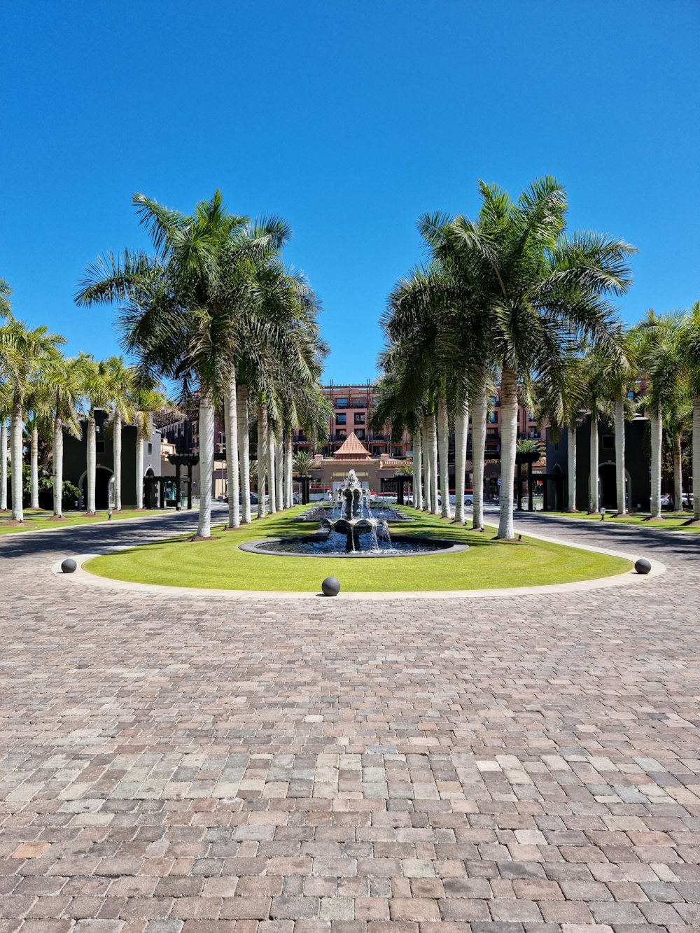 a fountain in a courtyard with palm trees and a building in the background