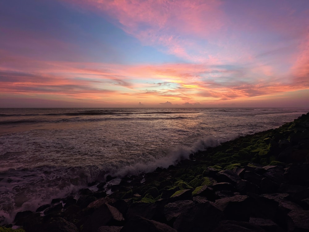 a rocky beach with a pink and purple sky