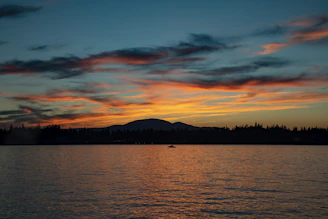 Sunset over a calm lake reflecting vibrant colors with a silhouette of a lone fisherman.